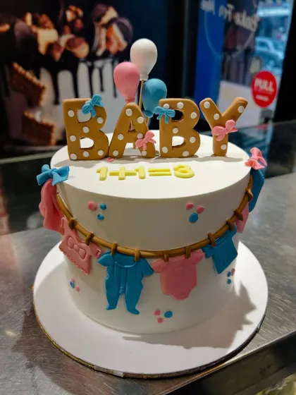 A cute baby shower cake with a clothesline of blue and pink baby clothes, and gingerbread-style "BABY" letters.