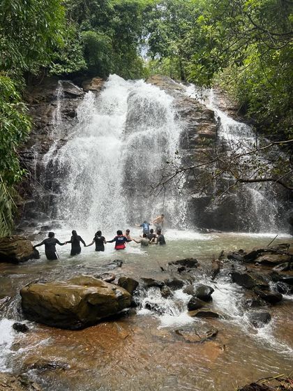 A group of friends holding hands and forming a chain in the waterfall, a symbol of the unity and fun we have on our trips.