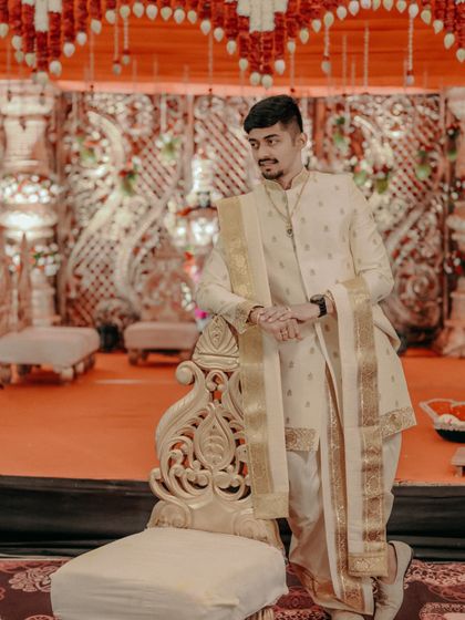 The groom posing with confidence by an ornate chair on the wedding stage.