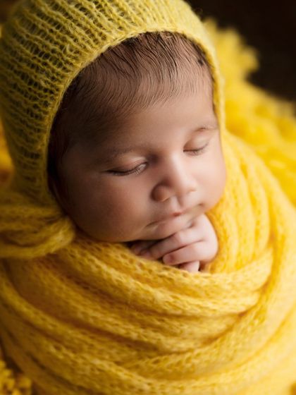 A close-up of a newborn wrapped snugly in a yellow knit, a perfect example of beautiful wrapping.
