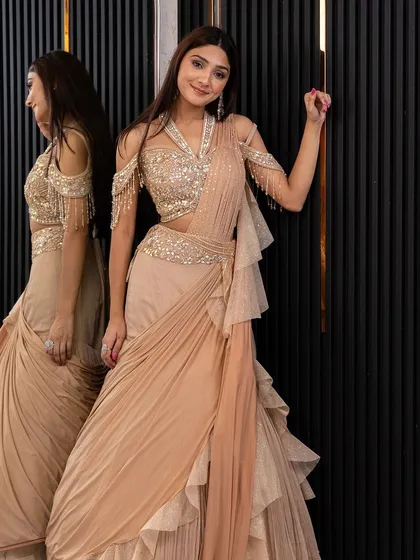 This beige ruffled and draped saree gown is the epitome of modern elegance. The embellished cold-shoulder blouse adds a touch of glamour, perfect for a reception.