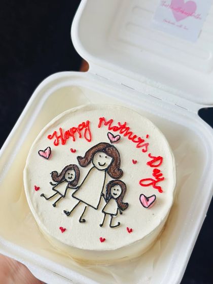 A truly personal touch for Mother's Day. This bento cake features a hand-drawn stick-figure portrait of a mother and her two daughters, making it a unique and heartfelt gift.