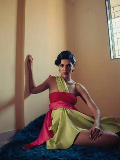 A seated pose from the 'two shirts' series, showing the draped dress in a moment of quiet. The natural light from the window creates a soft, contemplative mood.