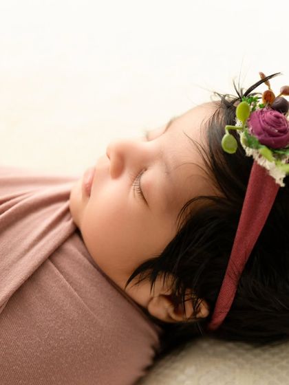 A detailed close-up of a sleeping newborn's face, focusing on their delicate features and a beautiful floral headband.