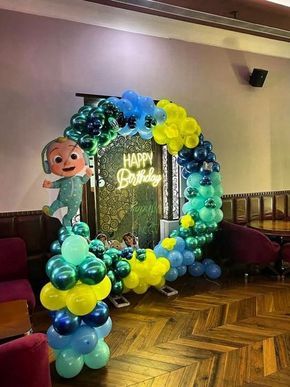 A Cocomelon-themed birthday decoration set up in a restaurant. The circular balloon arch and character cutout create a fun photo corner for guests.