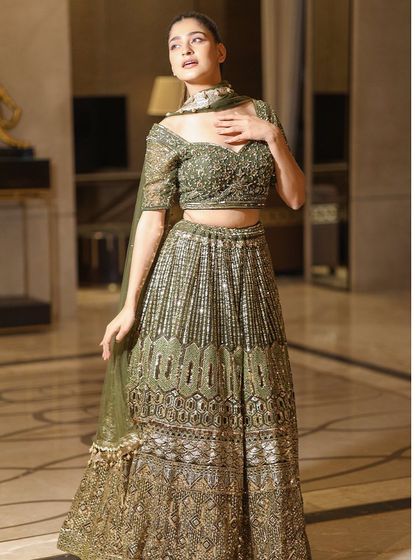 A full-length view of the olive green and gold lehenga, showcasing its flattering A-line silhouette and the rich, intricate embroidery that covers the entire skirt.