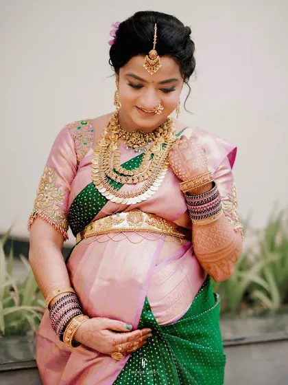 A classic portrait of a mother-to-be during her Seemantham ceremony. She gently holds her baby bump, adorned in a traditional silk saree and exquisite temple jewelry, embodying the grace of motherhood.