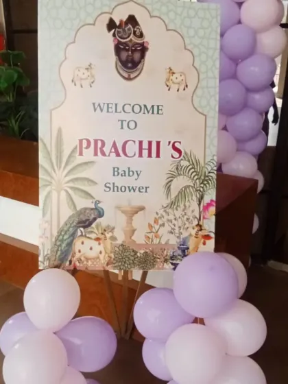 A close-up of the welcome sign for 'Prachi's Baby Shower'. The sign features beautiful traditional Indian artwork, including a peacock and Krishna illustration.