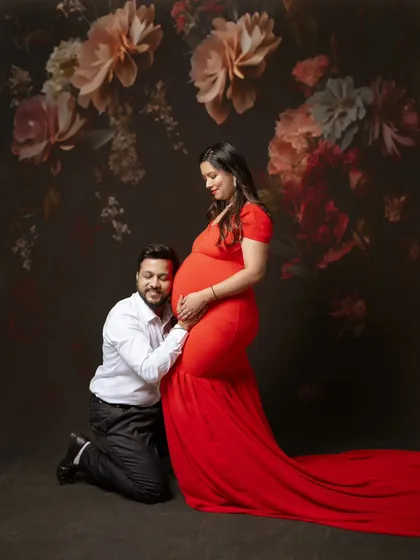 A classic and romantic maternity portrait. The vibrant red gown against a painterly floral backdrop creates a sense of drama and passion, while his gentle pose shows his adoration and support.