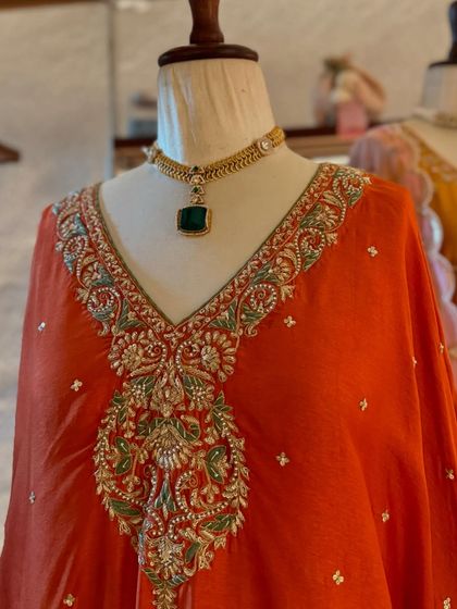 A vibrant orange kaftan with intricate silver and green embroidery, complemented by a stunning emerald necklace.