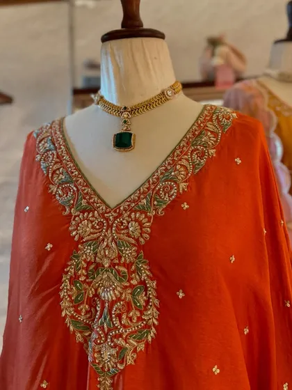 A simple yet elegant gold choker with a single emerald-green stone, perfectly complementing the heavy embroidery of this orange kaftan.