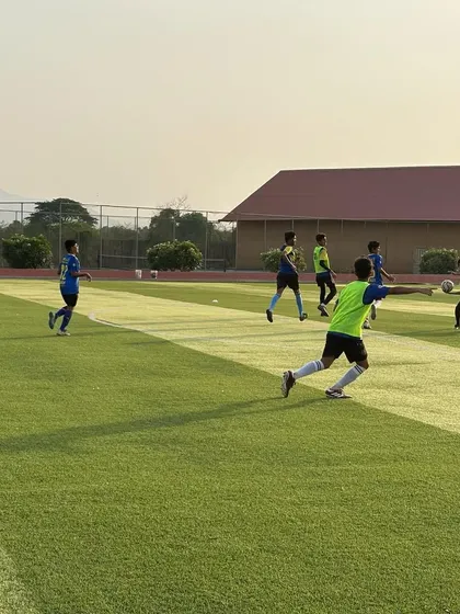 An evening training session in progress at the residential academy. The setting sun casts a golden light over the pitch as players engage in drills, showing that football is the start and end of every day here.