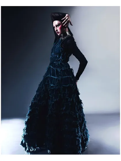 A full-length shot that captures the dramatic silhouette of the frayed denim gown. The pose is statuesque and powerful, fitting the avant-garde nature of the design.