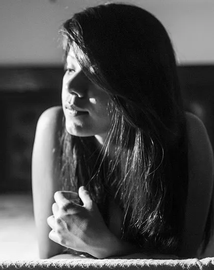 A woman lying on a bed, with soft sunlight streaming in. This black and white photo has a peaceful, lazy-afternoon feeling.