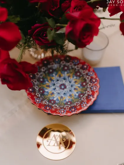 A custom gold coaster with the couple's monogram sits beside a colorful, hand-painted plate, showcasing the event's blend of personalization and artistry.