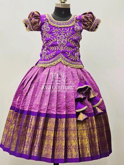 A grand Kanchi Pattu lehenga in purple and pink. The blouse has intricate embroidery, and the skirt has a unique side tassel design.
