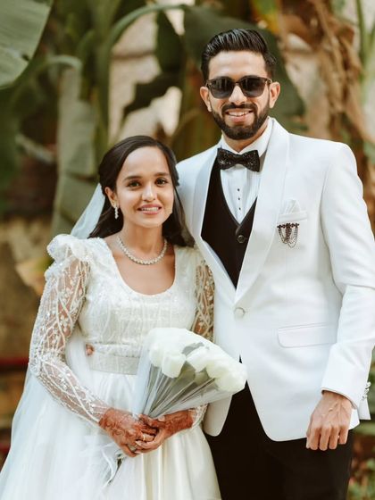 A classic portrait of the stylish couple. The groom's white tuxedo and the bride's elegant gown with lace sleeves are the epitome of wedding day sophistication.