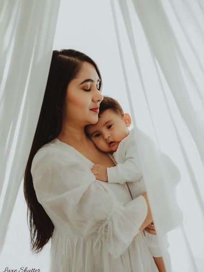 A mother and child embraced in a hug, framed by soft white curtains. This artistic shot has a dreamy, ethereal quality.