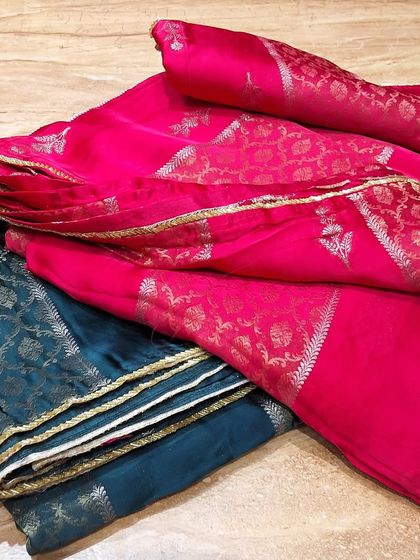 A selection of soft silk fabrics in vibrant pink and deep teal. These materials with delicate gold zari work are ideal for creating custom blouses, kurtis, or sarees.