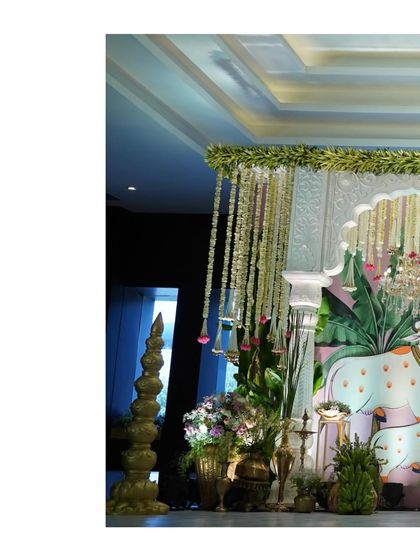 A partial view of the Pichwai stage, showing the intricate details of the painted backdrop, pillars, and hanging floral elements.