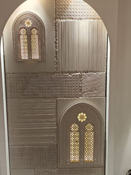 An arched wall niche featuring a patchwork of textured stone and backlit jali windows. This design adds depth and a sense of heritage.