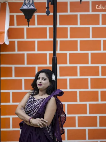 A chic portrait against an orange brick wall. The simple background makes the subject and her purple saree-gown stand out.