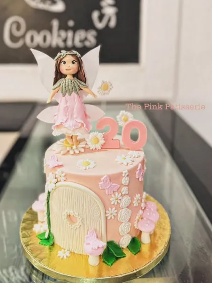 An enchanted fairy garden cake for a 20th birthday. The cake features a fairy house door, delicate flowers, mushrooms, and a beautiful fairy topper.