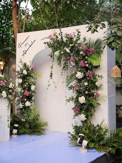 A modern and minimalist decor setup for a wedding. The clean white arches adorned with flowers create a chic and sophisticated look against the green backdrop.