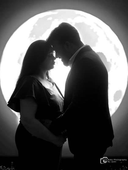 A dramatic black and white silhouette of an expecting couple against a moon prop in the studio. This style focuses on their connection and the shape of the baby bump.