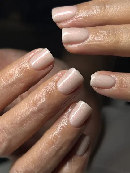 A soft, shimmery vanilla nude polish on natural square nails. This subtle sparkle adds a touch of elegance to a classic everyday look.