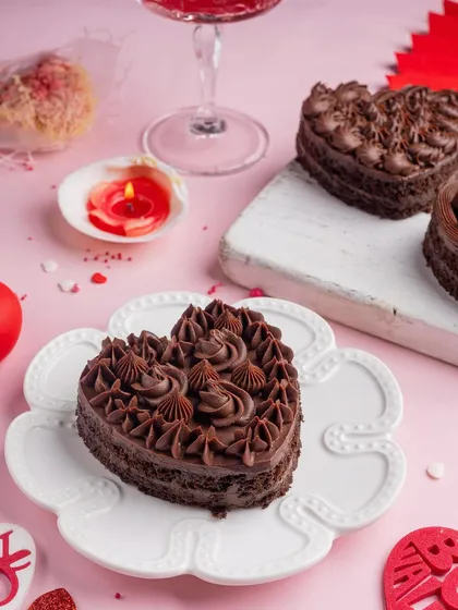 A rich, heart-shaped chocolate cake, perfect for a decadent Valentine's treat. The moody lighting and single red candle create an intimate and romantic vibe.