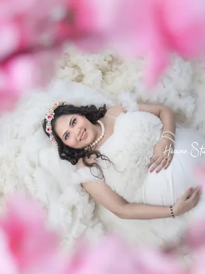 Dreaming of the little one. This creative shot, framed by soft pink flowers, captures the mother-to-be in a moment of serene contemplation, looking absolutely angelic in a white ruffled dress.
