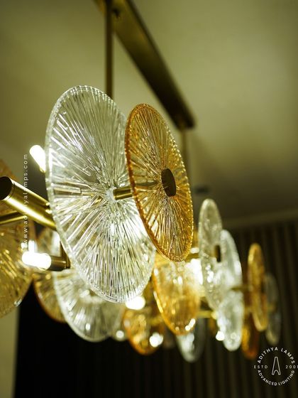 A linear chandelier featuring an arrangement of clear and amber-tinted textured glass discs. This fixture provides both direct and ambient light, adding a layer of sophistication and warmth to dining areas and boardrooms.