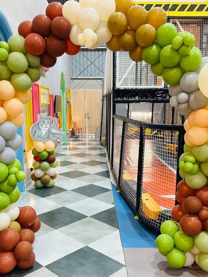 A fun balloon arch in earthy tones for a cat-themed party, set up in a kids' play area.