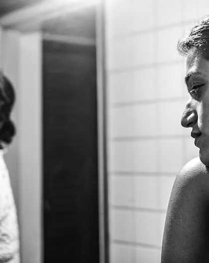 A woman looking at her reflection in a mirror. This black and white shot is introspective, exploring themes of self-perception and identity.