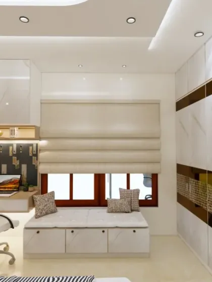 A bright and modern bedroom with a window-side seating nook. The design features a large wardrobe with a marble and gold-finish, and a functional study area.