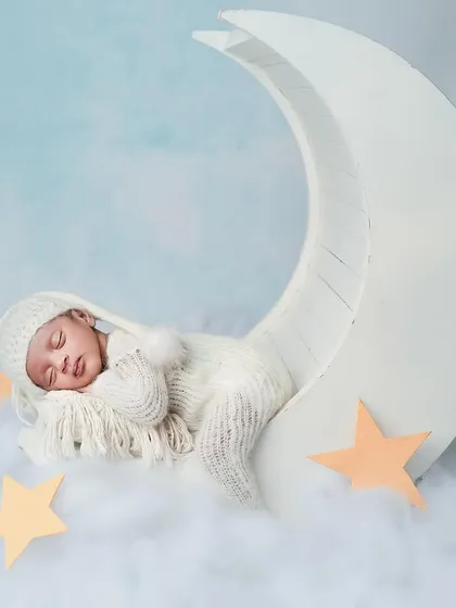 Our little boy sleeping peacefully in his own dreamland. The crescent moon prop and soft clouds create a magical and serene atmosphere for a newborn portrait.