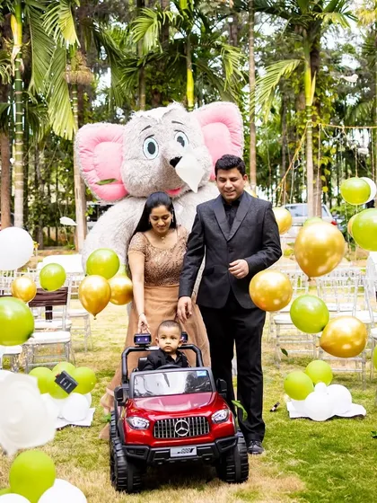 The birthday boy, Shourya, making a grand entrance in a toy car, accompanied by his parents and a large elephant mascot.