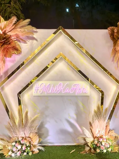 This bohemian photo booth features a custom neon hashtag against a clean backdrop. The geometric gold frames and dried floral arrangements add a trendy and personalized touch.