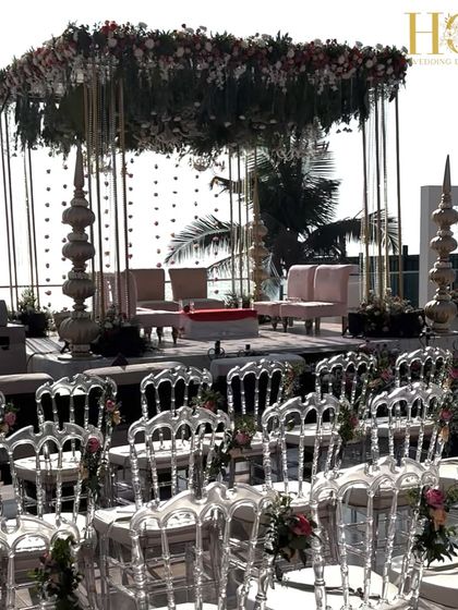 A wide shot of the seaside wedding mandap, showing the guest seating with ghost chairs that don't obstruct the beautiful ocean view.