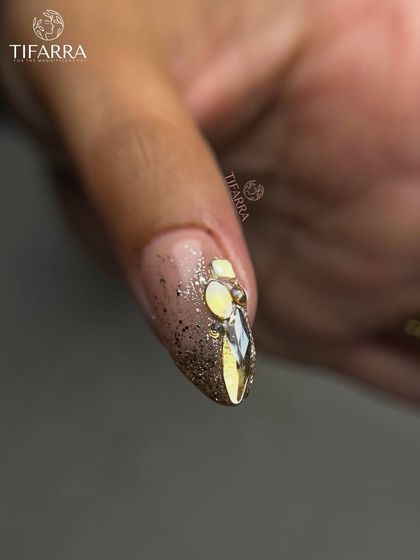 A close-up of a nail tip adorned with carefully placed faceted rhinestones, adding a touch of sparkle to the intricate gold and glitter design.