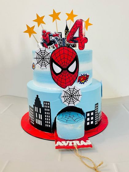 A full view of the two-tier Spiderman cake. The bottom tier features a city skyline, while the top has the iconic Spiderman mask and other comic book elements.