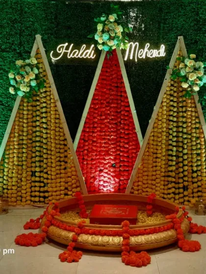 This is a vibrant Haldi and Mehendi stage I created. It uses a traditional green grass wall backdrop with geometric structures made of marigold flowers and a custom neon sign, perfect for pre-wedding ceremonies.