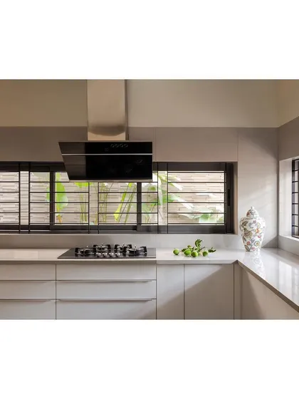 The kitchen in the "Solid | Void | Solid House" is designed as a functional and elegant space, with clean white cabinetry and windows that look out onto a green wall.
