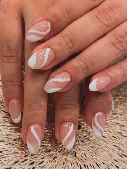 A chic and modern design on short, almond-shaped nails. This set features a sheer nude base with bold white swirls, creating a clean and artistic negative space look.