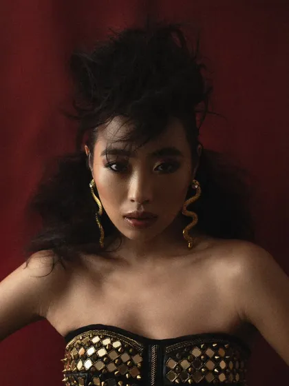 A beauty editorial focused on creating sculptural, avant-garde hair. This portrait uses a rich red background and focused lighting to highlight the texture of the hair and the snake-like earrings, creating a look that is both powerful and ethereal.