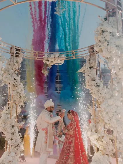 A spectacular Varmala moment set against a grand palace backdrop in Rajasthan. The explosion of rainbow-colored smoke and sparklers creates a truly cinematic and unforgettable frame, highlighting our expertise in capturing large-scale destination weddings.