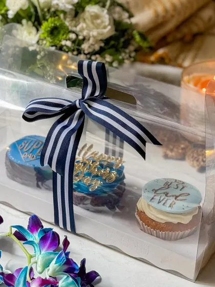 A clear gift box showcasing a trio of my Father's Day cupcakes, elegantly tied with a striped ribbon. This highlights the beautiful presentation of my gifts.