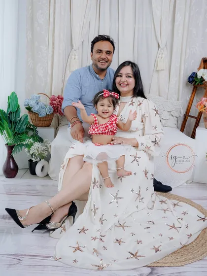 A playful family moment captured in the studio. The little one is the star of the show, waving happily from her mother's lap in this cheerful family photo.