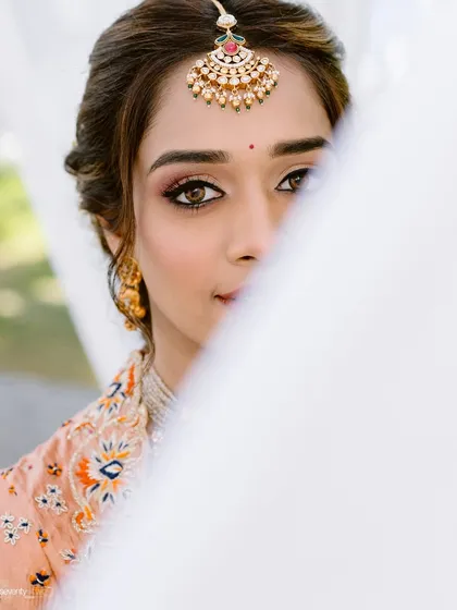 A stunning bridal portrait from a Haldi ceremony, with the bride's face partially veiled, drawing attention to her expressive eyes and beautiful maang tikka.